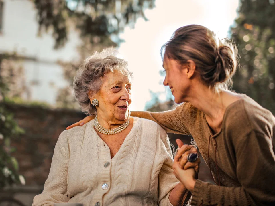 An adult daughter holding hands with her mother in a garden